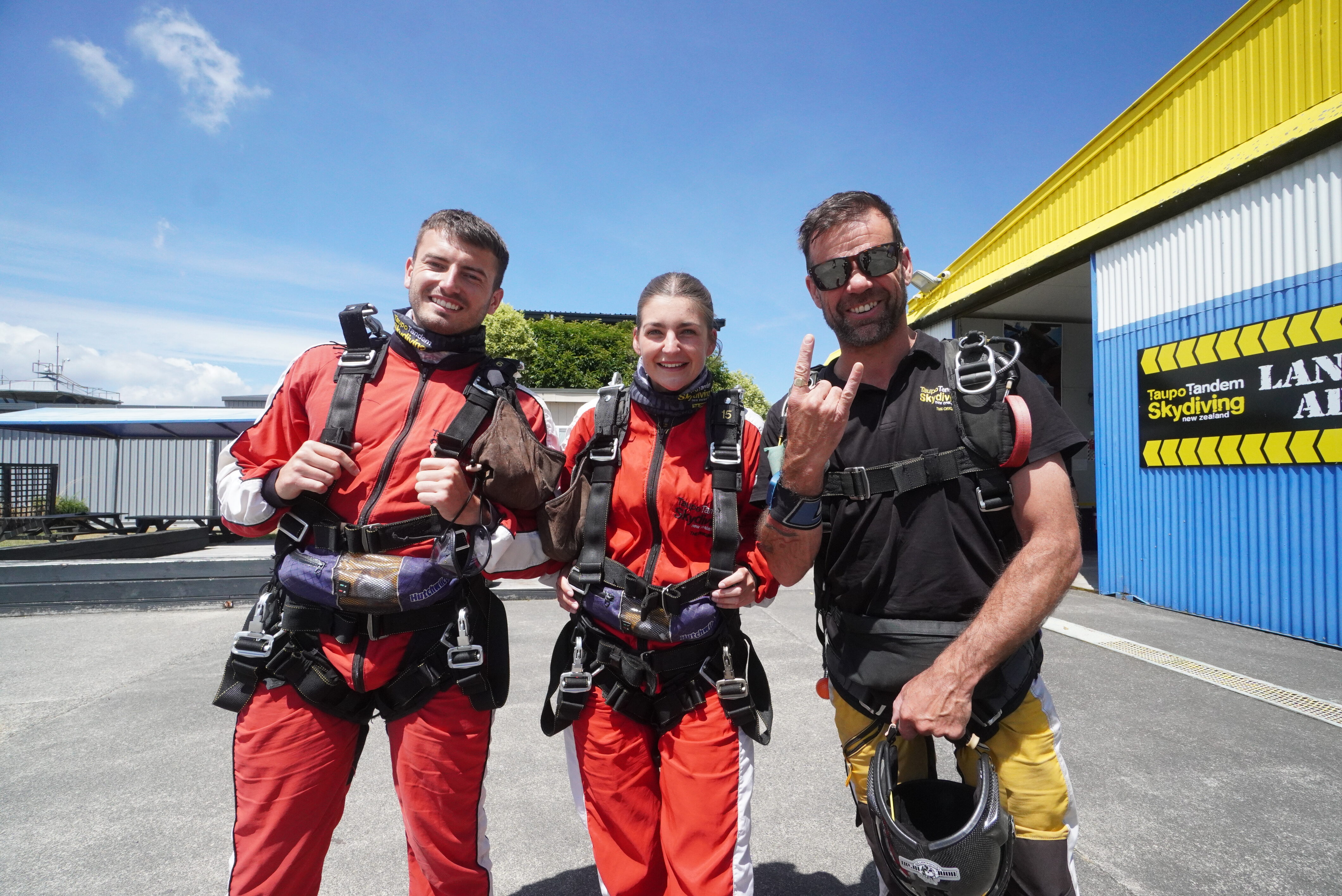 Two tandem customers and a tandem master in jumpsuits, all excited for their skydive!